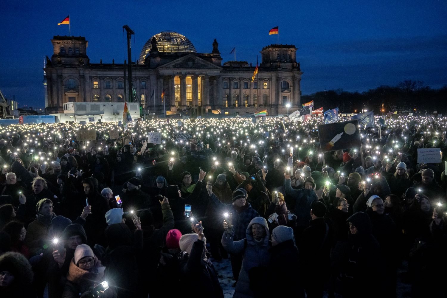 A crowd of people hold up their cellphone flashlights in front of a parliament building. It is dark out.