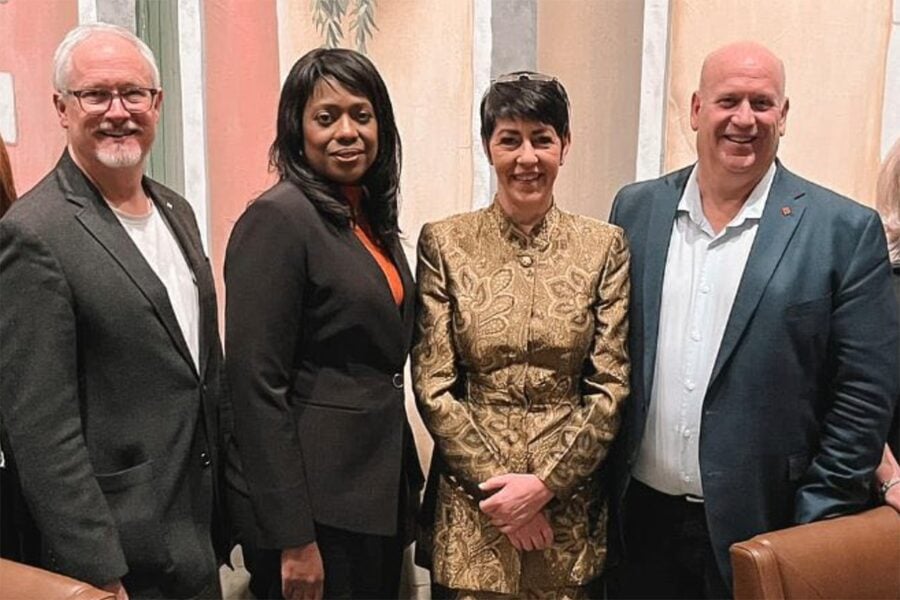 Four people pose in a group. From left, a white man with thinning white hair, a Black woman with long black hair, a white woman with short dark hair and a bald white man.