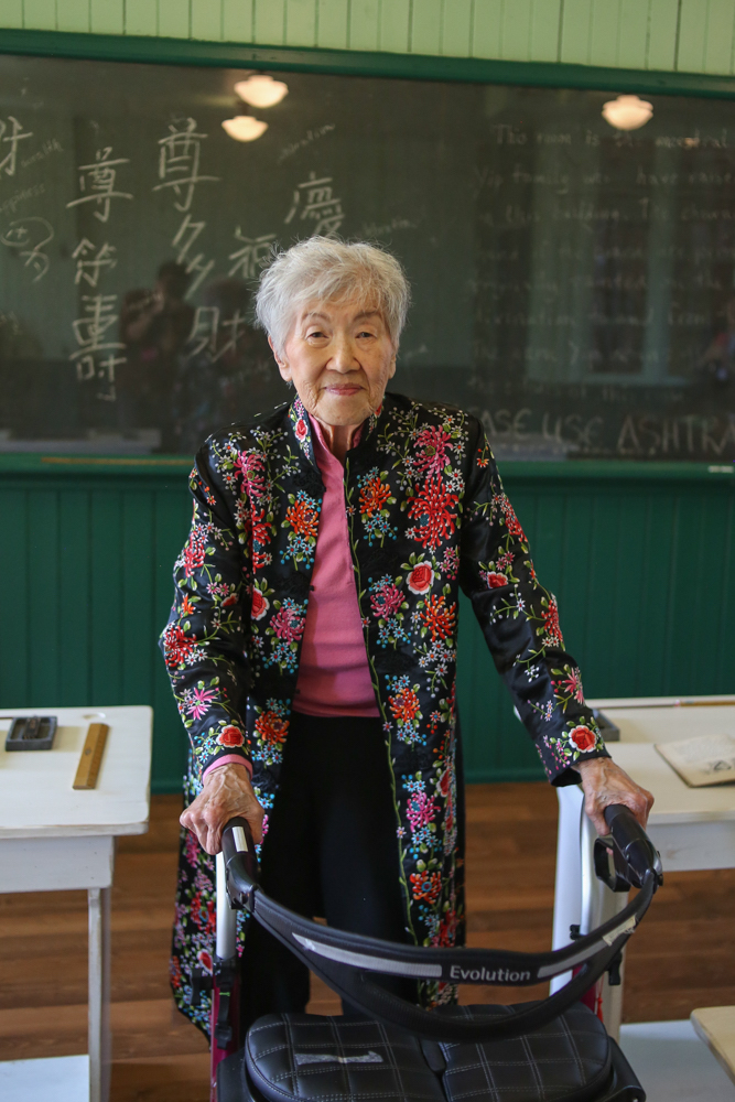 An old ethnically Chinese woman in a walker in an old classroom.