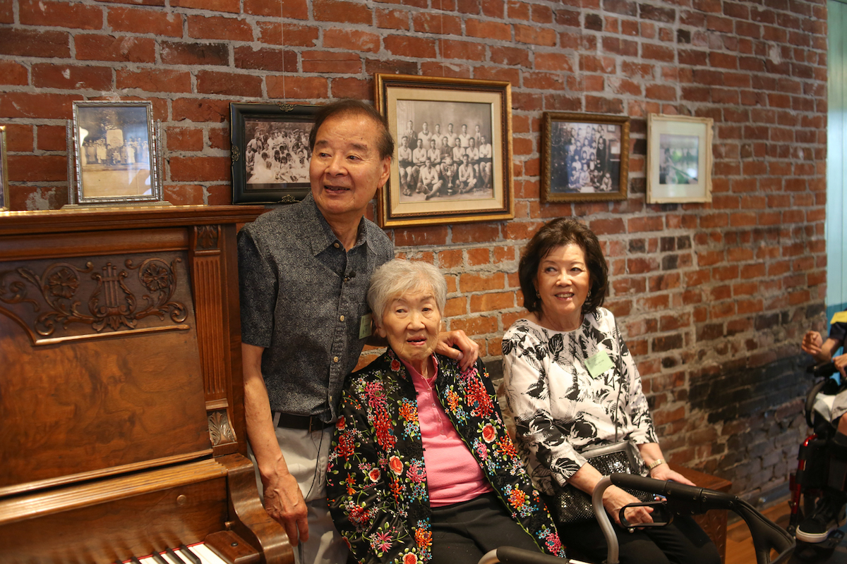 Three Chinese seniors in a room with old black-and-white pictures.