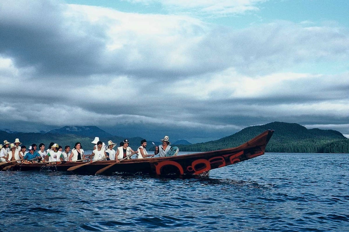 A number of people in a large, traditional red-cedar canoe in the ocean.