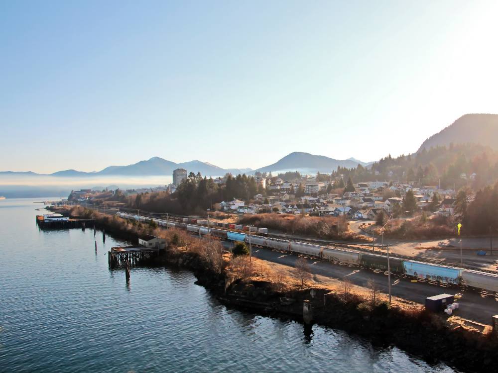 A coastal community with a train in the foreground, ocean on the left and mountains behind.
