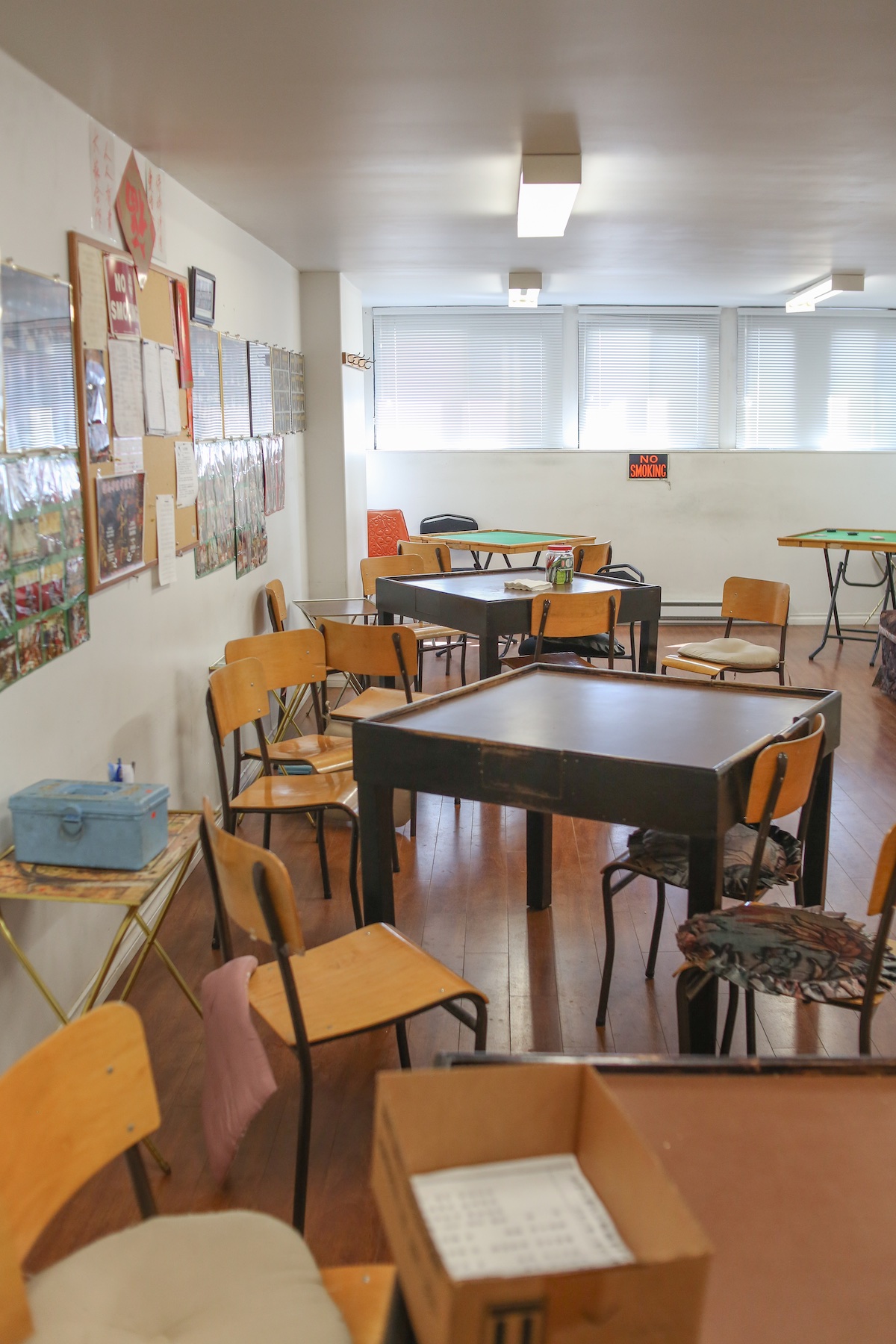 A brightly lit indoor space features several wooden classroom-style chairs and a square table used for playing mah-jong.