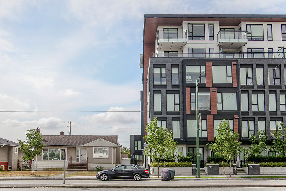 A stucco bungalow sits beside a modern six-storey residential building.