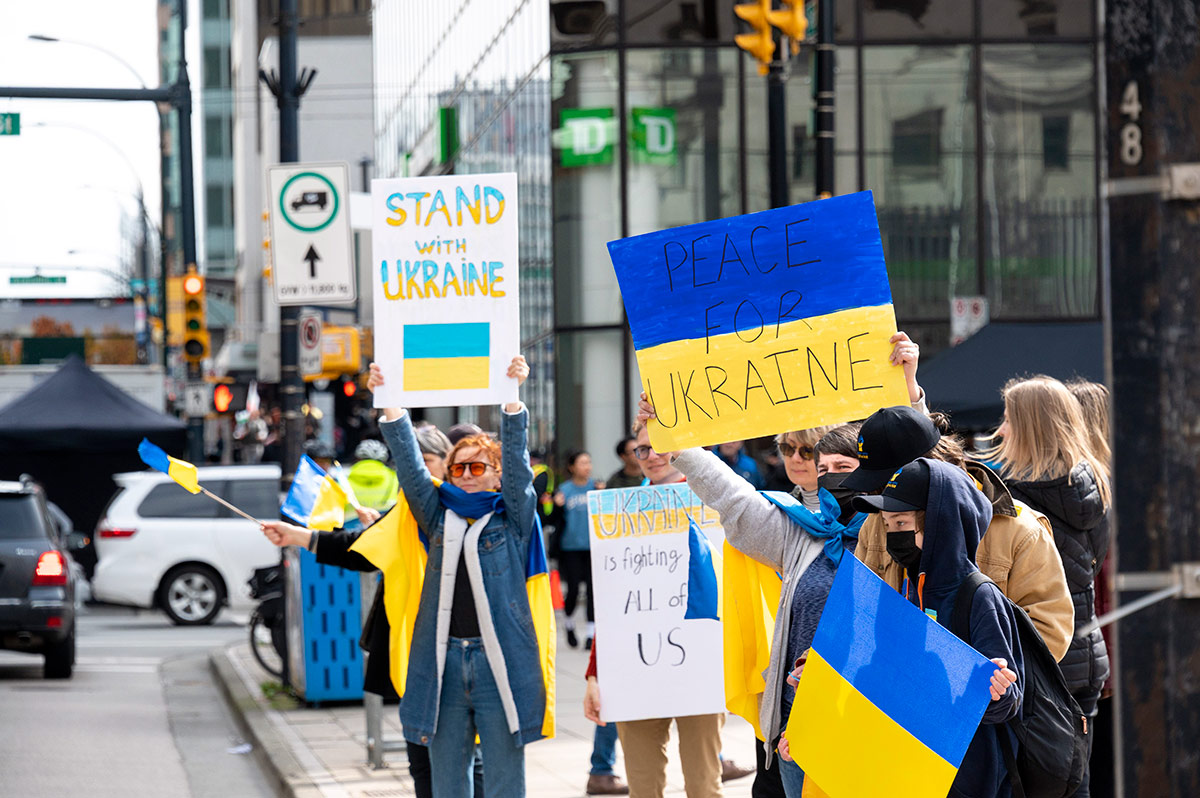 People standing beside a street in Vancouver hold signs saying 'Peace for Ukraine' and 'Stand with Ukraine.'