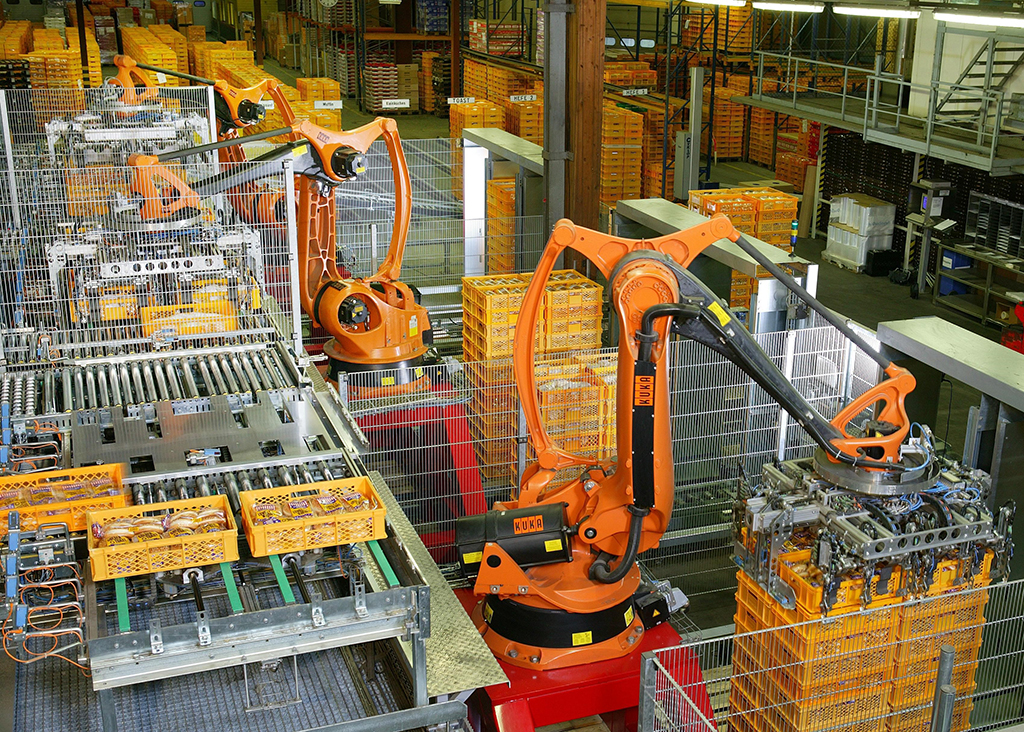 Machines with yellow crane-like arms package bread in an industrial factory.