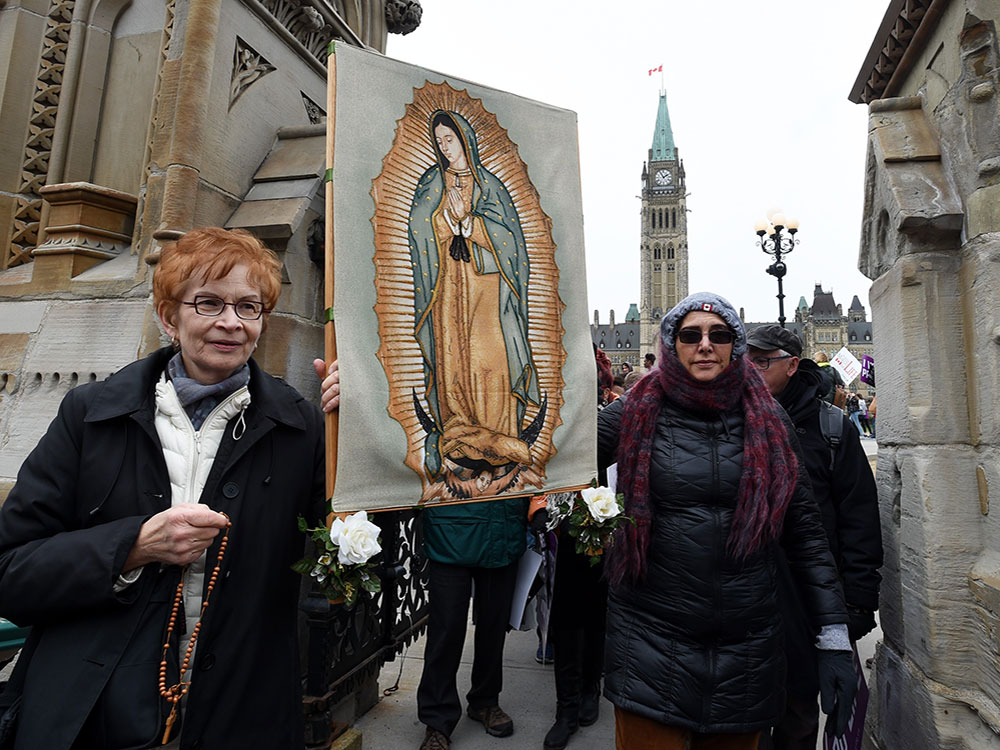 Two protesters hold up a Catholic saint sign with the Parliament building in the background.  