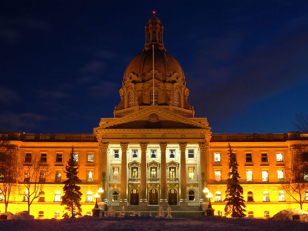 A domed legislative building with columns is lit golden against the dark night sky.
