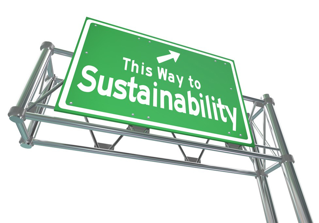 A freeway sign says “This way to sustainability” in white letters against a green background with an arrow pointing up and to the right.