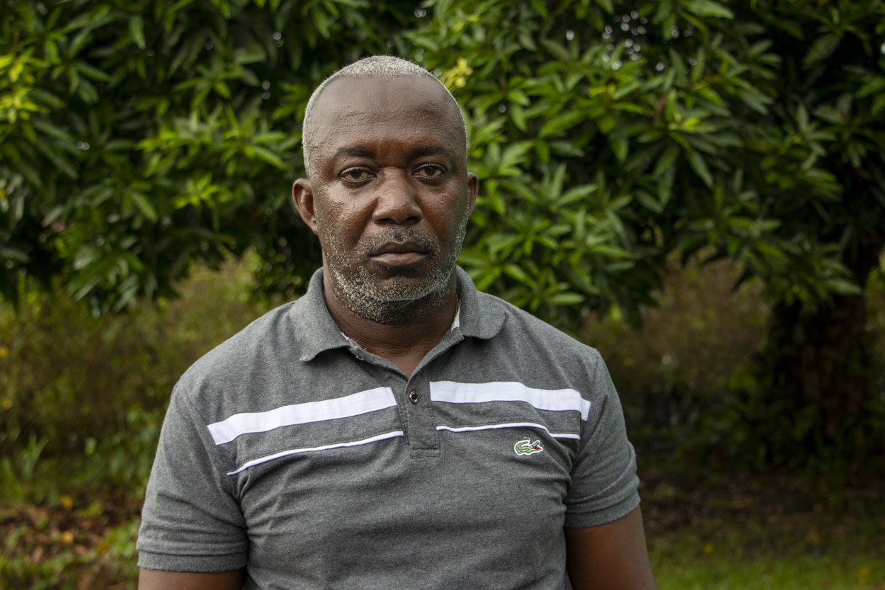 A man facing the camera with lush vegetation in the background.