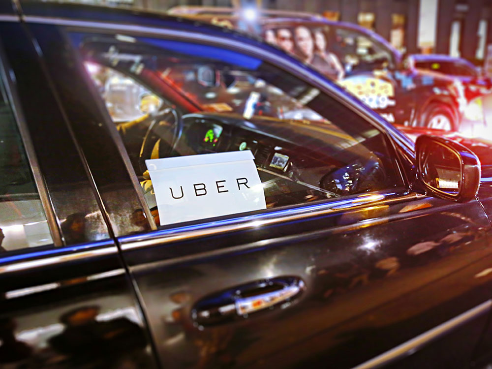 An Uber sign is seen on the front passenger seat window of a black car.
