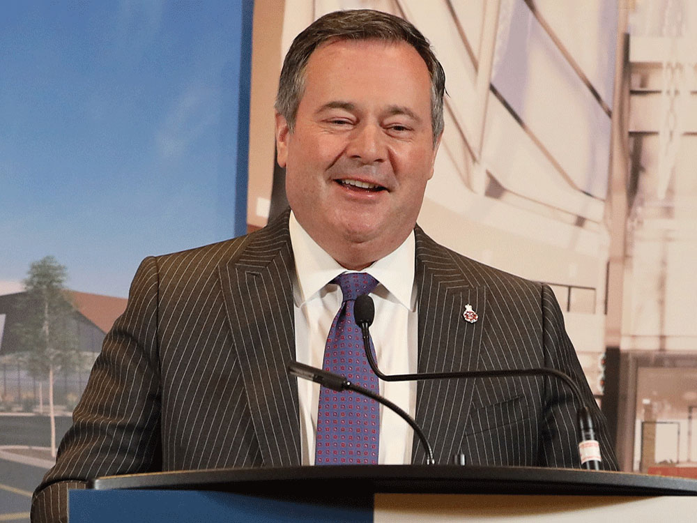 Jason Kenney, grins as he speaks at a podium, wearing a gray striped suit and blue tie.