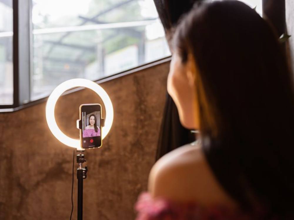 A young woman making photo or video content for social media with smartphone and light of ring lamp.