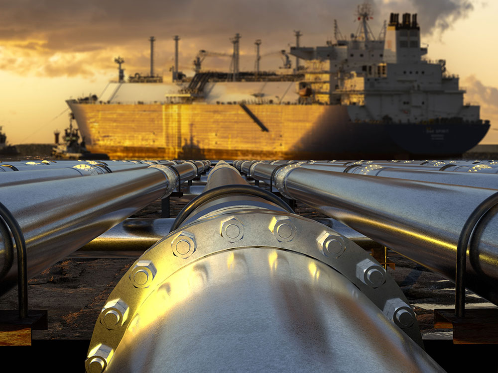 Shiny silver pipelines lead toward an LNG ship in the evening sun.