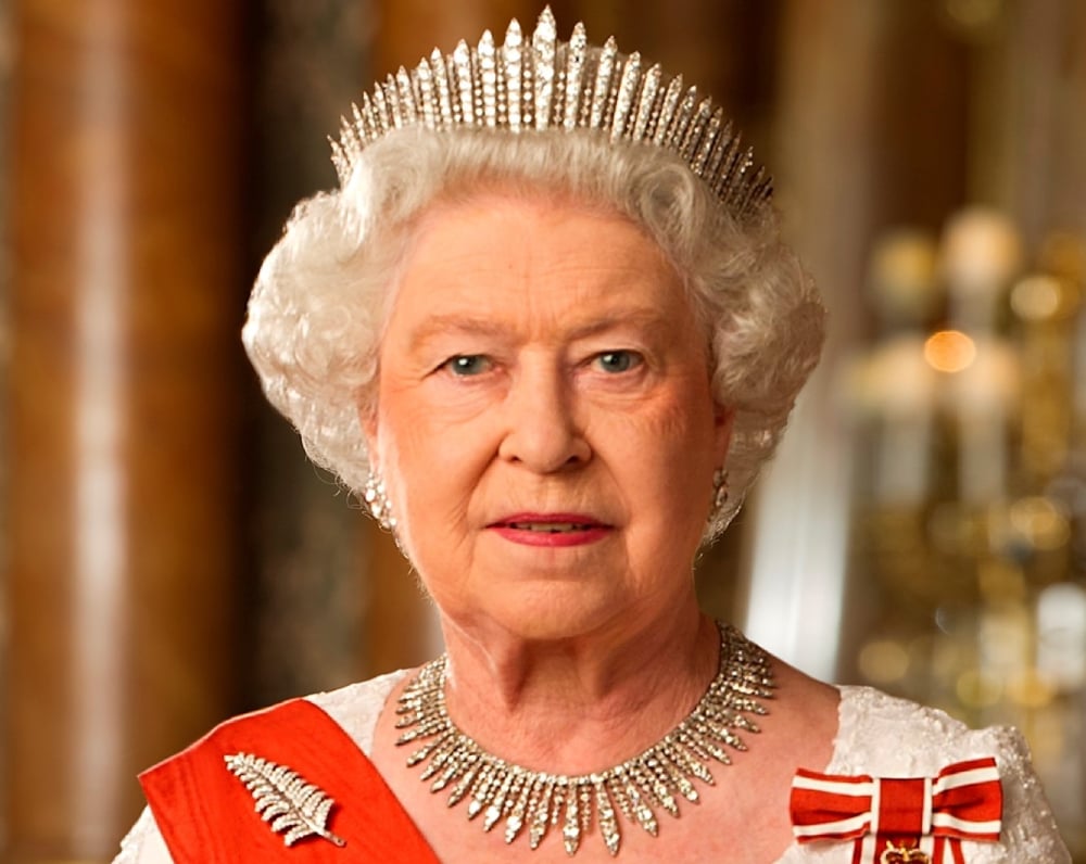 A formal portrait of Queen Elizabeth in late-middle age staring directly into the camera, her hair white, wearing a diamond encrusted crown and necklace and white dress.