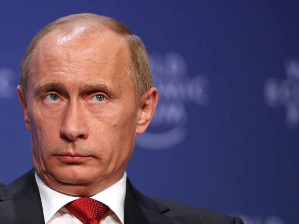 A close up of a tie-wearing, white, rounded, late middle aged face, eyes shifting to the viewer’s right — the familiar visage of Russian leader Vladimir Putin.