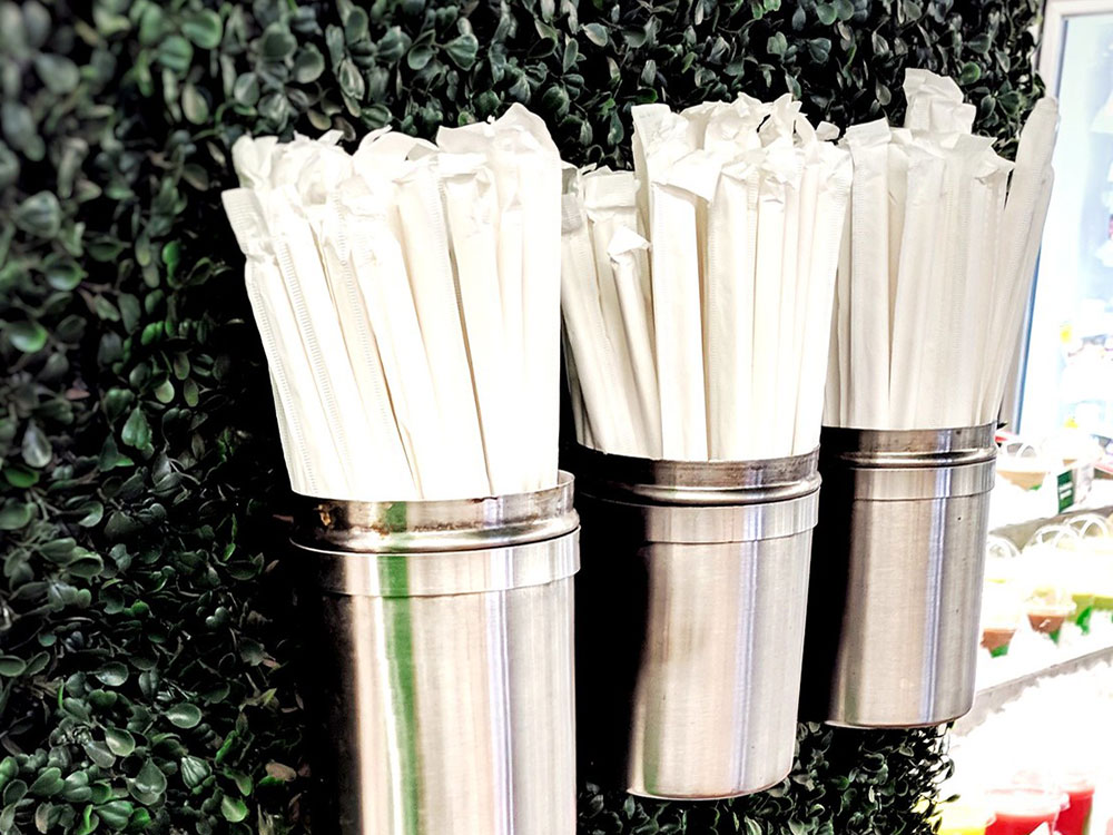 Three metal cups affixed to a wall hold packaged paper straws.