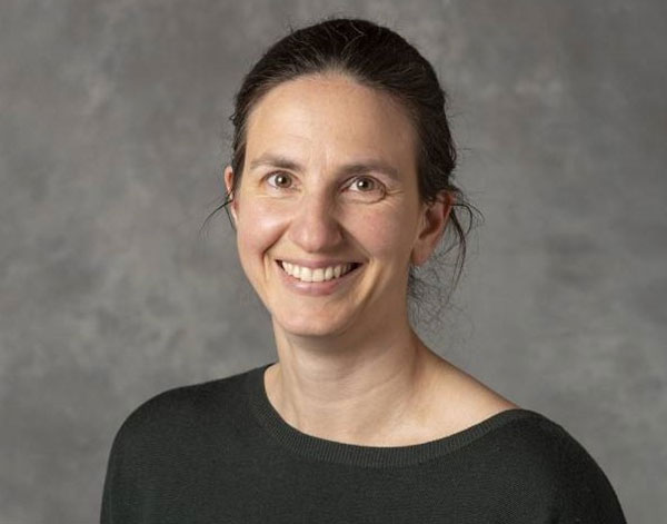 A woman with pulled back dark hair and wearing a black collarless short smiles at the camera.