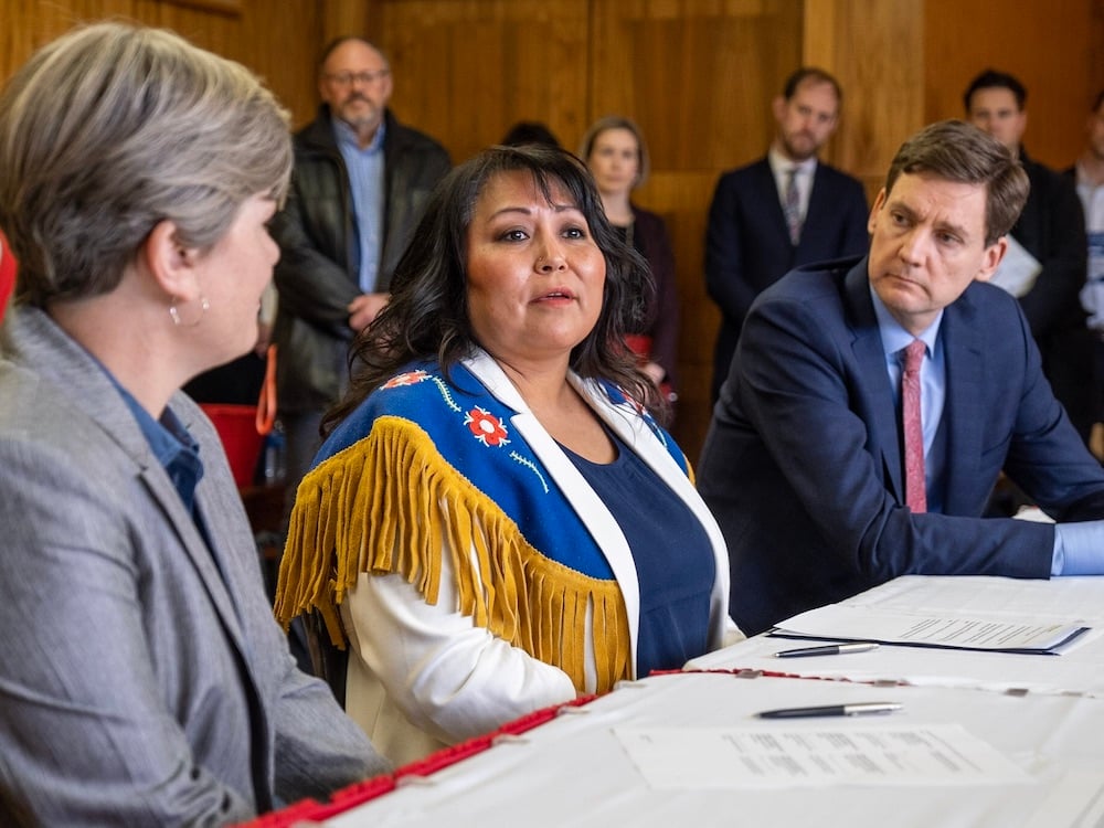 Three people sit at a long table angled towards the camera. B.C. Energy Minister Josie Osborne is in the foreground, Chief Judy Desiarlais is centre, and Premier David Eby is furthest back.