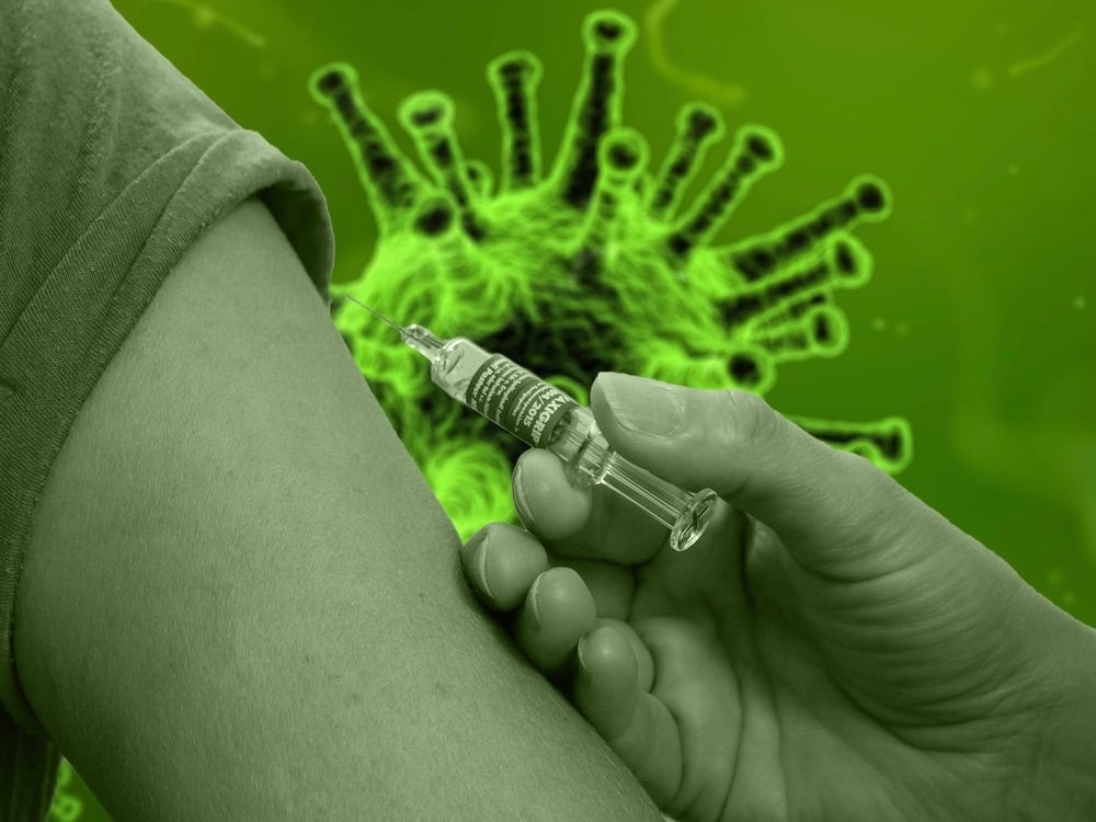 A stylized green-tinted image shows a COVID virus in the background and a hand giving an injection in the foreground.