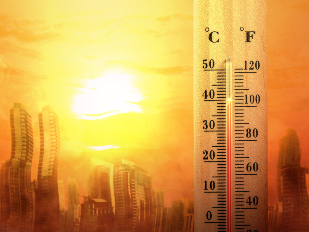A thermometer is juxtaposed against a yellowy urban skyline and bright sun. The building seem to be melting.