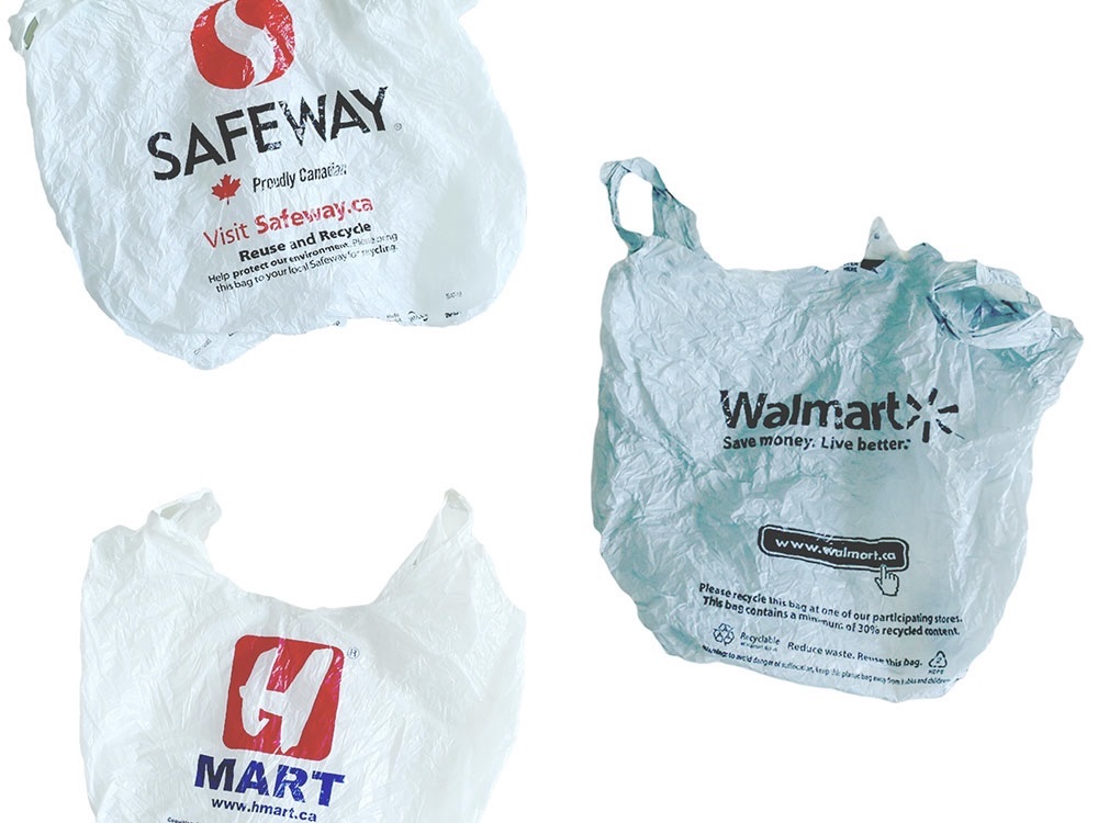 Three plastic grocery bags against a white background. Clockwise from top: a white Safeway grocery bag with a red logo, a grey Walmart grocery bag with black text; a white H-Mart grocery bag with a red logo and blue text.