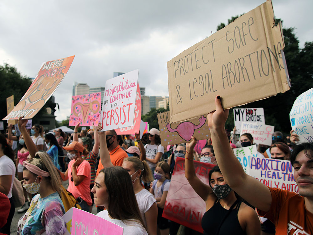 Protestors hold signs with messages such as ‘Protect Safe and Legal Abortions’ and 
‘We’re Not Property.’