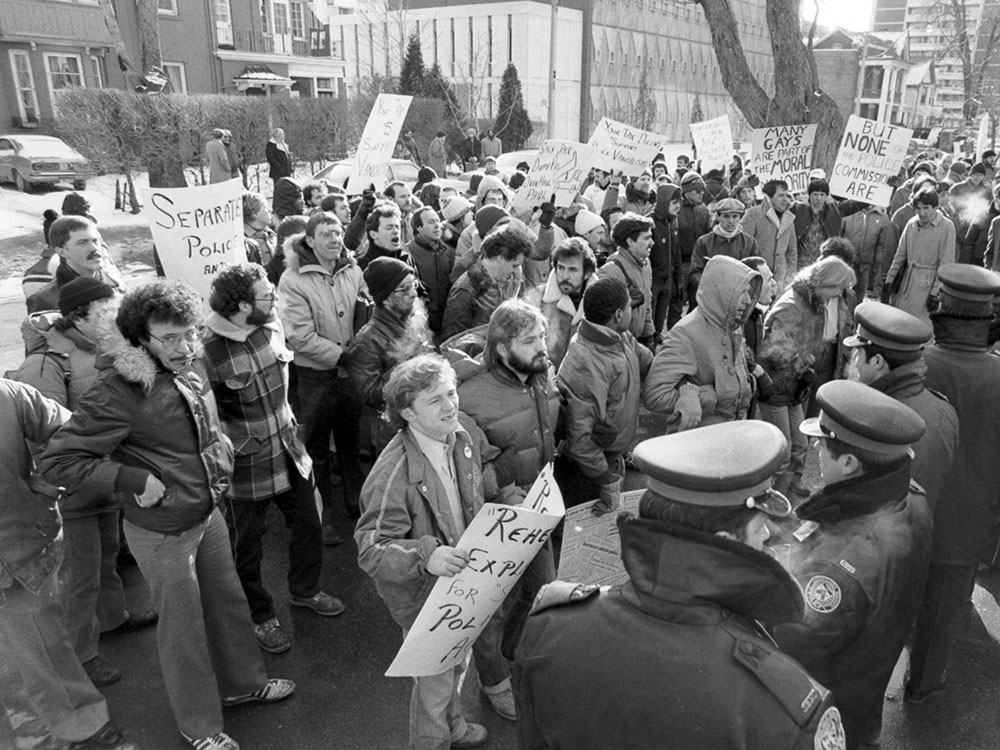 A black-and-white photo shows protesters facing a line of police officers.