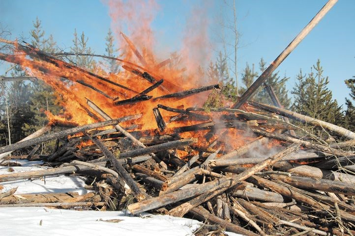 A pile of branches and stumps are being burned in a snowy clearcut.