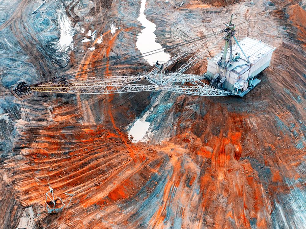 A machine leaves grooves in bare, red earth as it mines for rare metals.