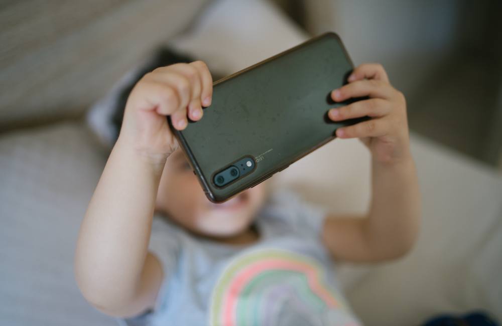 A child reclines on a couch looking at a smartphone. 