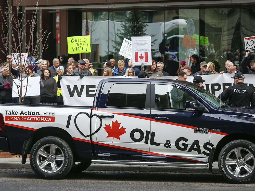 A black-and-white truck bears the slogan “I love Canadian oil and gas” as protesters hold signs calling for pipelines to be built.