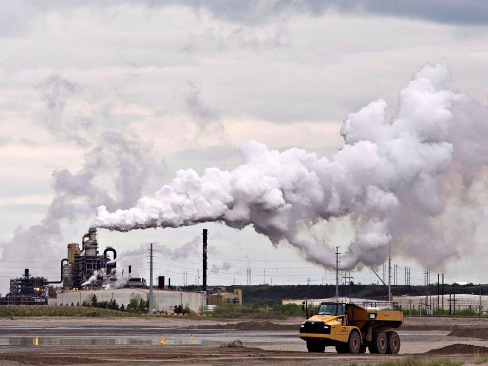 White steam or smoke billows from a stack and extends above an industrial setting, with a large yellow dump truck in the foreground.