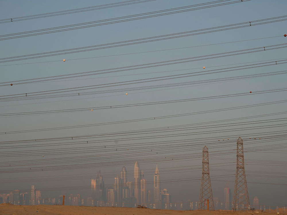 Power lines and transmission towers in front of a hazy skyline of Dubai.