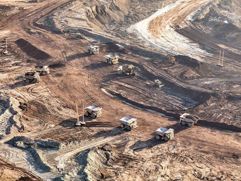 Giant dump trucks and diggers work on a vast area of the oilsands already stripped of dirt in an aerial photo.