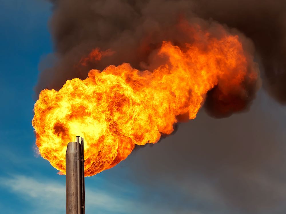 A flaring stack rises into the sky, with giant yellow and orange flames and dark smoke.