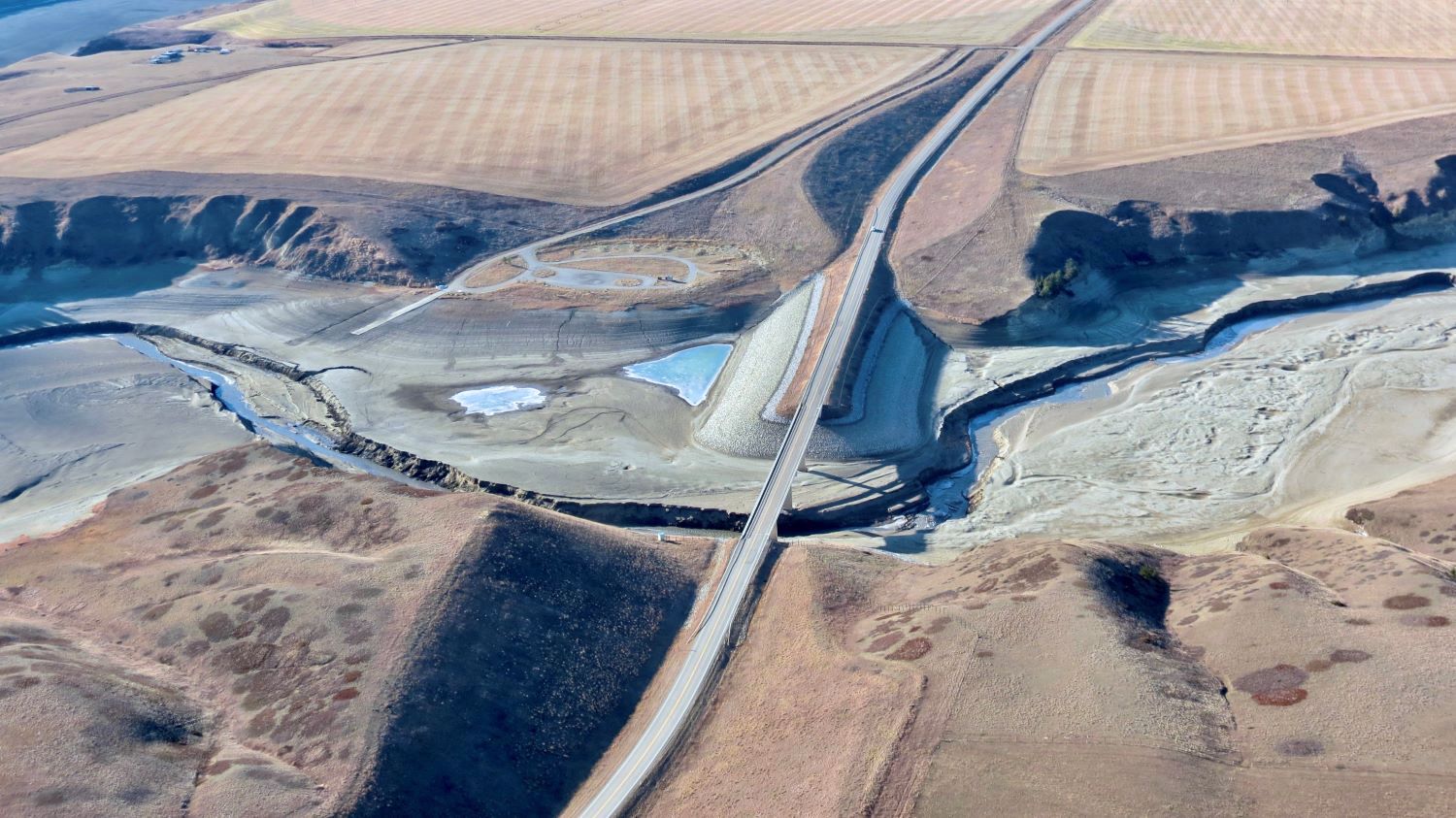 An aerial photo shows an overpass crossing what was a wide river and now is all but empty of water. A large buildup of silt is to the right of the overpass.