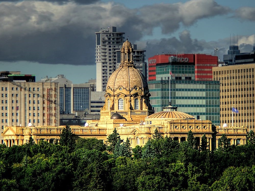 The Alberta Legislature Building. Sunlight shines on it, but dark clouds loom.