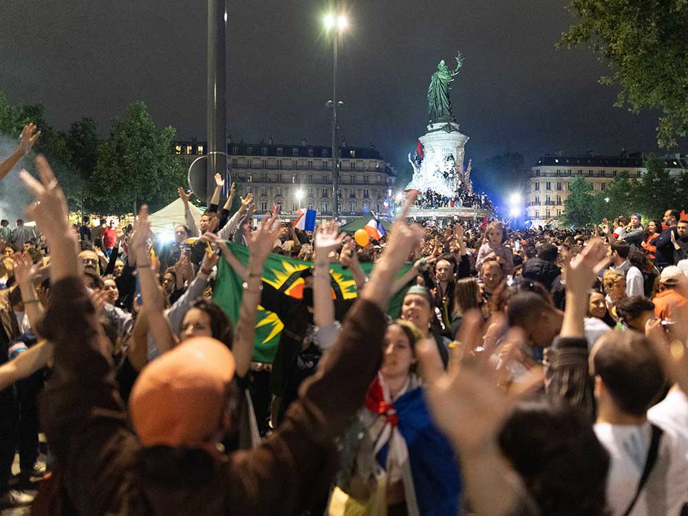 Signatories of the New Popular Front of the French Left smile and stand together in a chaotic photo on the steps of a large house in Paris. They are all dressed formally or semi-formally in an array of colours.