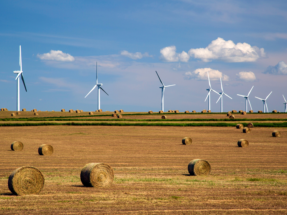 Renewable energy wind turbines in a harvested agricultural field with bales hay in the Canadian prairies of Alberta, Canada.