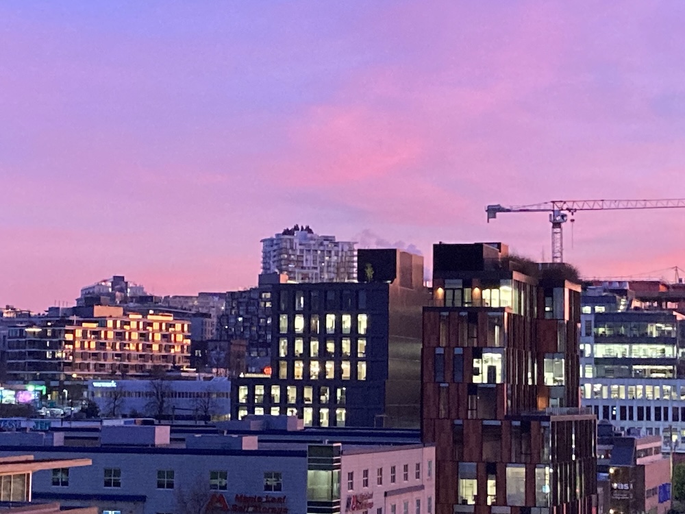 A view of new low-rise condominium buildings on a slope at sunset. The buildings stand against a pink and purple sky.