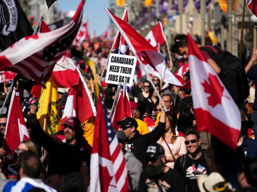 A crowd of people march on an urban street, holding Canadian flags and signs.