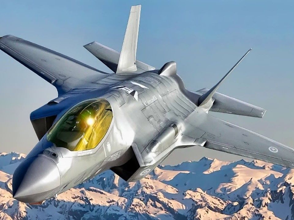 A sleek silver-grey fighter jet airborne over a snowy mountain range.
