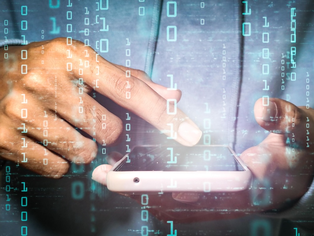 Fingers hover over a cellphone, while digital data is superimposed on the image.