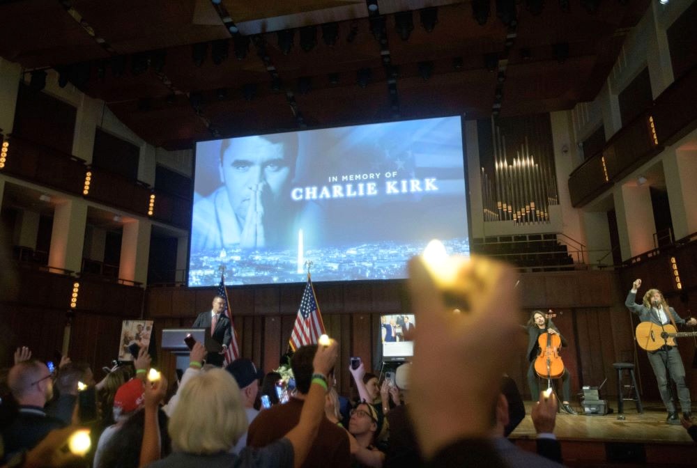 The image of Charlie Kirk is projected on a screen as people hold up lighters.
