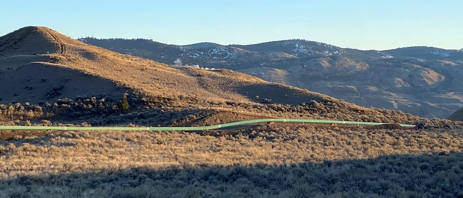 An exposed green pipeline lies atop an arid landscape on a sunny winter day.