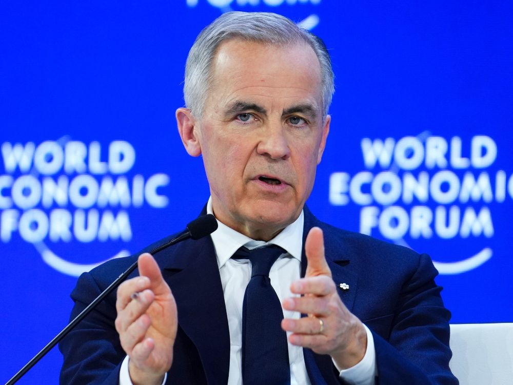 Mark Carney stands at a lectern, gesturing, in front of a blue background.