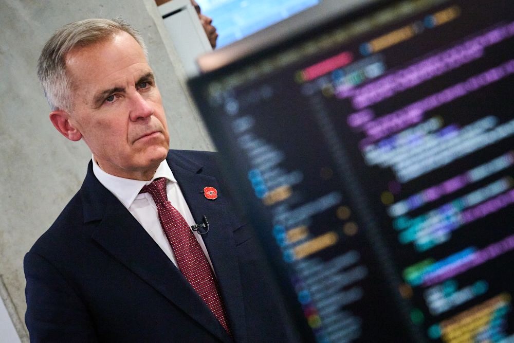 A grey-haired white man has an intent expression on his face. In front is a computer screen with lines of colourful out-of-focus characters.