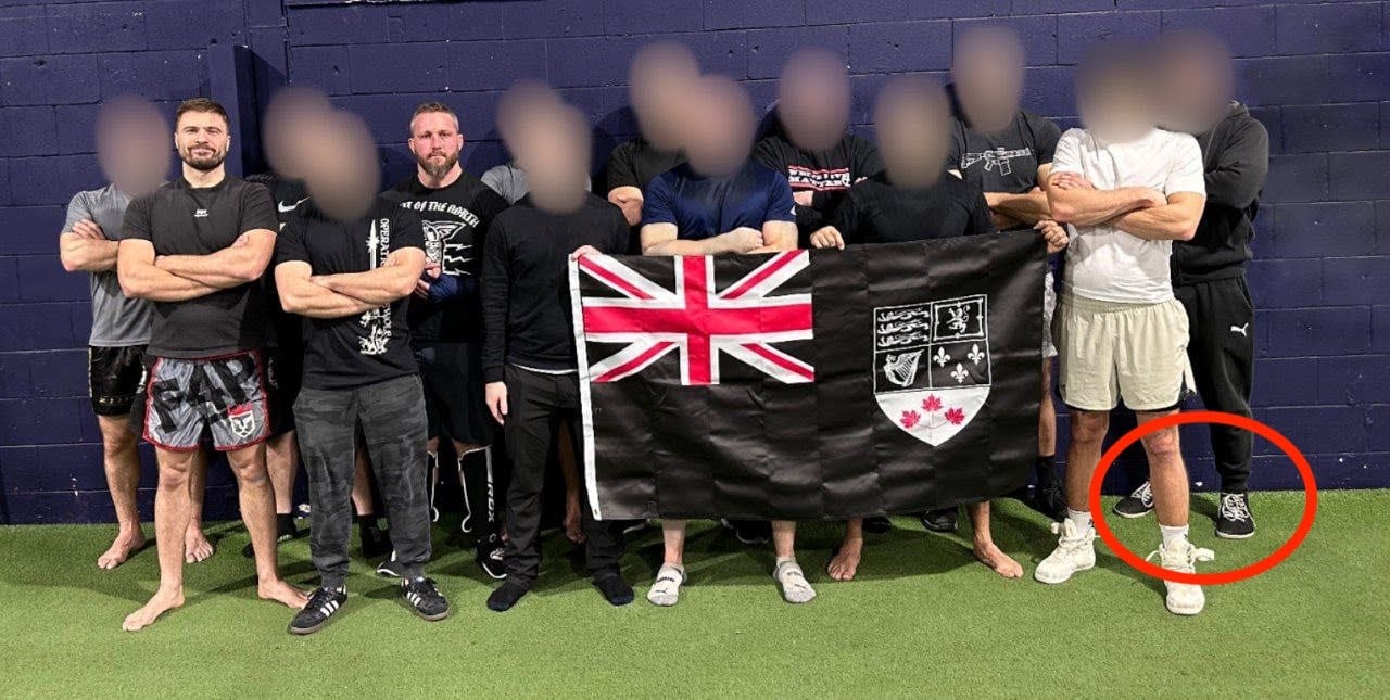 A row of eleven men at a gym. All but two of the men have their faces blurred. A red circle outlines the shoes of the man standing at the right edge of the photograph.