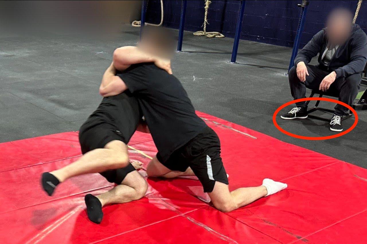 A photo of two men wrestling on a red mat; both have their faces blurred. Another man can be seen sitting in a chair. A red circle indicates his shoes, which match the shoes of the man seen in the previous two photos.